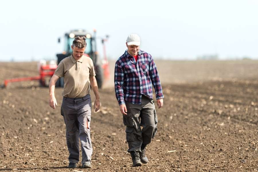 Aides Agriculteurs bénéficiant d’aides financières pour leurs cultures Deux agriculteurs inspectant un champ labouré avec accès aux aides financières