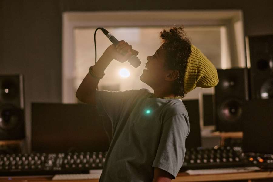 Artiste féminine en pleine session d’enregistrement vocal en studio professionnel Jeune chanteuse avec bonnet jaune chantant avec émotion au microphone dans un studio d'enregistrement