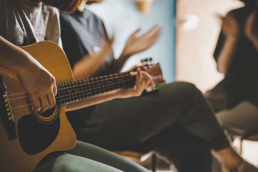 Jeune femme jouant de la guitare acoustique entourée d'amis dans une ambiance intimiste