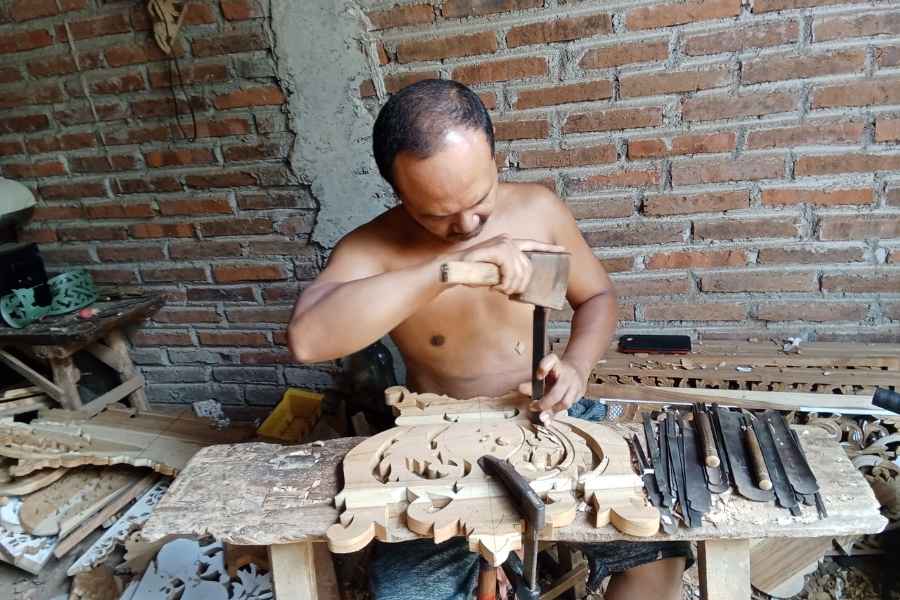 Artisan sculptant le bois avec outils traditionnels dans son atelier