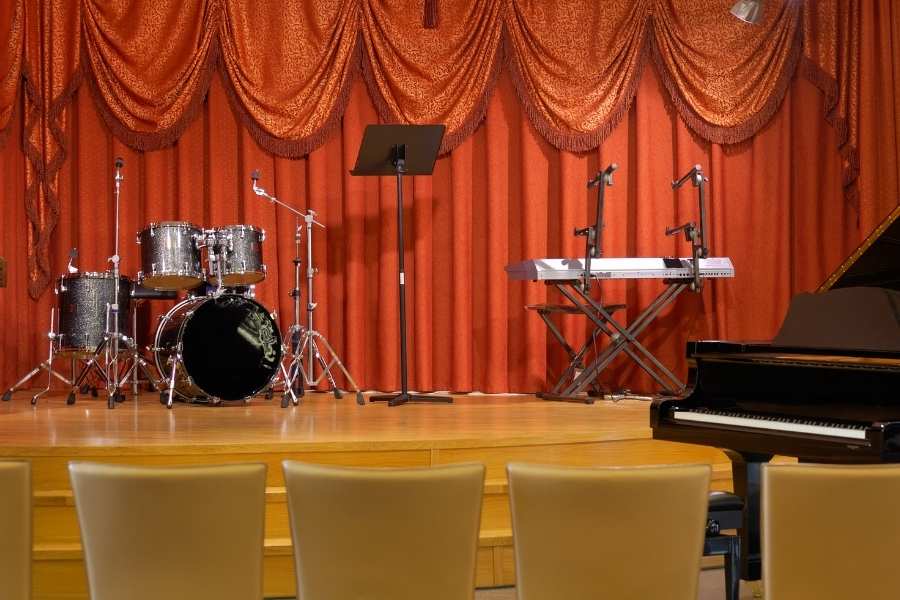 Installation scénique professionnelle prête pour un spectacle musical Scène de concert avec batterie, synthétiseur, piano et microphones devant un rideau rouge