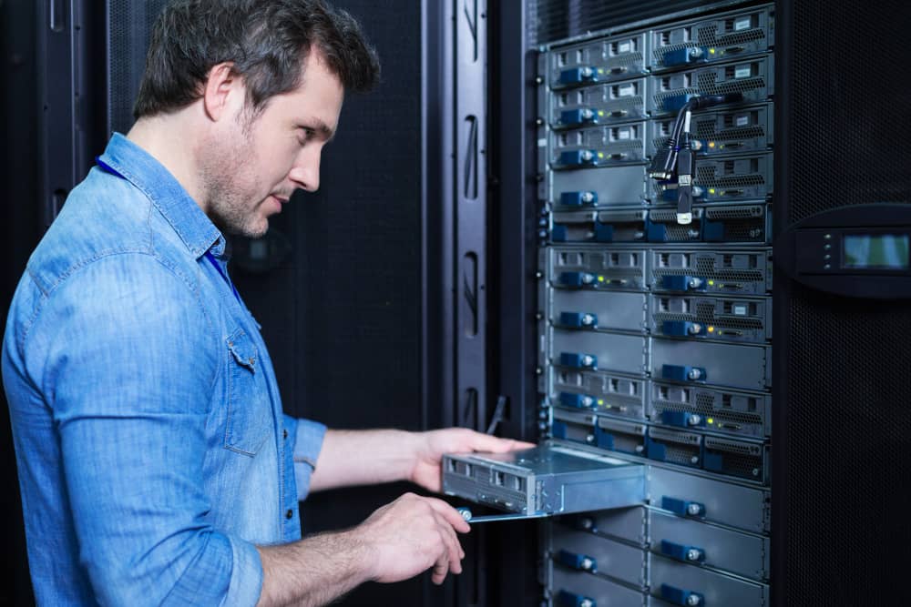 Installation et maintenance d’un serveur NAS de stockage. Technicien insérant un disque dur dans un rack de serveur NAS ou de stockage de données en salle serveur.