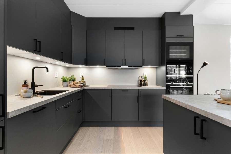 Une cuisine fonctionnelle moderne de couleur noir mat avec de nombreux rangements et un éclairage LED intégré.