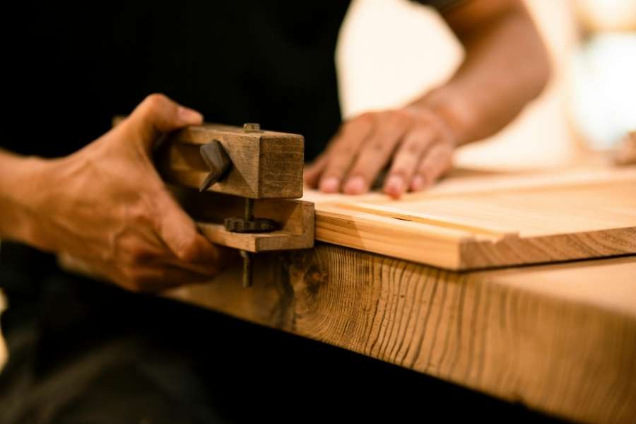 Un artisan utilise un serre-joint pour assembler deux planches de bois dans son atelier.
